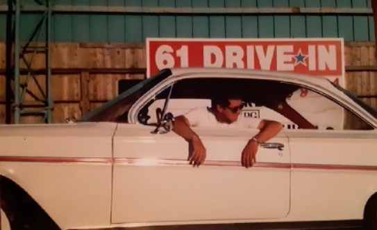 Young man sitting in his 1961 Chevy Bel Air at a drive-in theater, reflecting his lifelong passion for classic cars.