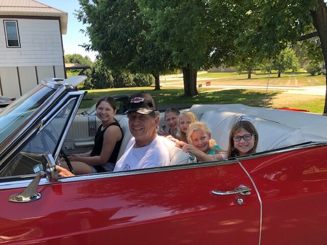 My father driving his restored 1965 Chevy Super Sport convertible with his grandchildren on a summer day.